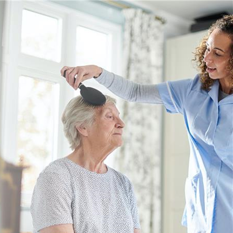 Domiciliary care worker brushing an old woman's hair in her bedroom