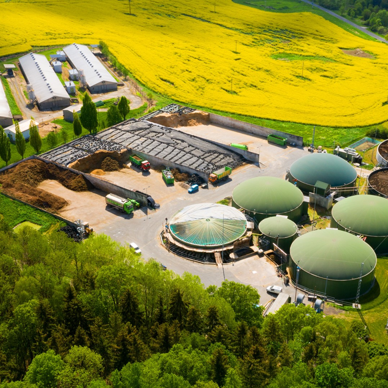 Aerial view of a farm facility featuring anaerobic digestion tanks and food waste disposal areas, surrounded by green fields and agricultural buildings.