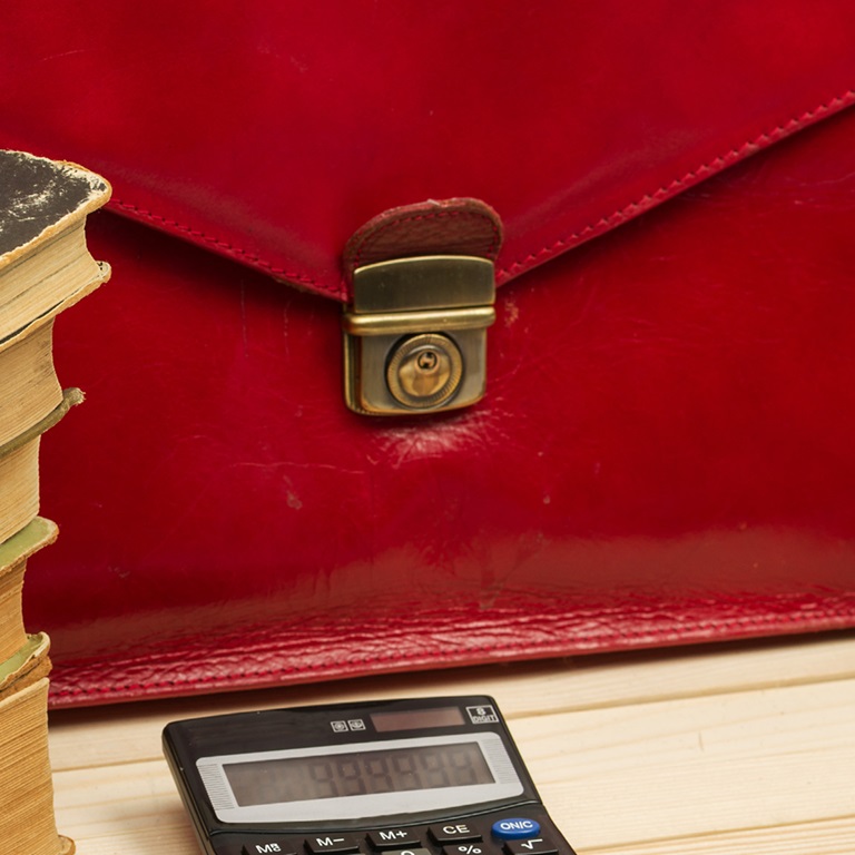 Close up of red briefcase on a desk with piles of books and a calculator